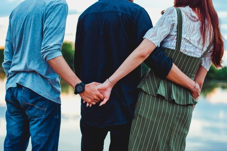 Three people standing with two holding hands behind ones back.